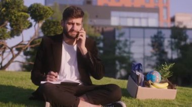 Genç bir ofis çalışanı işten kovulduktan sonra iş yerindeki çimlere oturur ve eşyalarını alır. Birini arar ve deftere bazı notlar yazar.