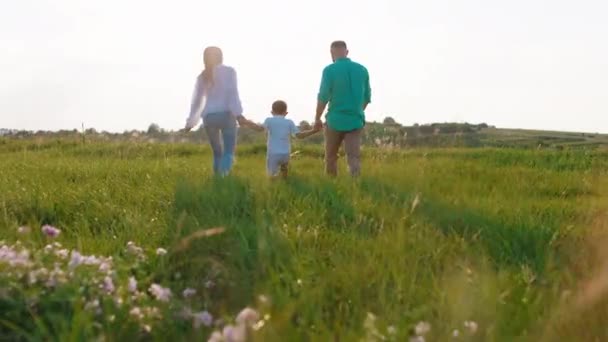 Familia feliz al atardecer caminando por el campo y disfrutar del momento juntos padres jóvenes y su hijo juntos exceso de tiempo — Vídeos de Stock