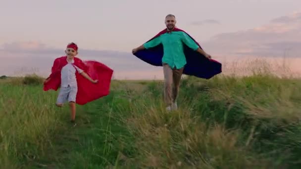 Correndo veloce bambino e suo padre indossano tute supereroi in mezzo alla natura al tramonto si divertono molto insieme — Video Stock