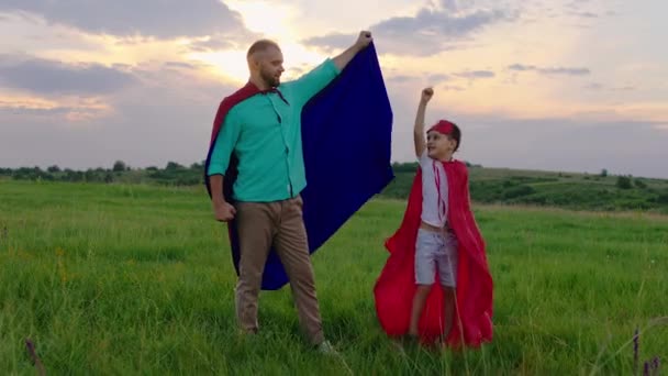 Glücklicher Papa und sein aufgeregter süßer kleiner Sohn genießen den Moment zusammen in der Natur, während sie in roten Anzügen in Superhelden spielen — Stockvideo