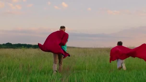 En la naturaleza feliz papá y su pequeño hijo corriendo rápido a través del campo verde y sintiéndose emocionados de pasar tiempo juntos — Vídeos de Stock