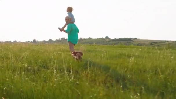 Šťastný čas v přírodě dobře vypadající muž a jeho legrační roztomilý malý syn na zádech běží všechny dohromady přes zelené pole po nich běží roztomilý malý pes — Stock video