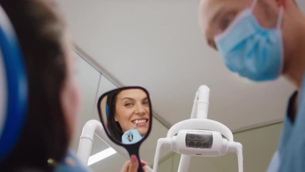 Стоматолог мужчина и его пациент обсуждают вместе о цвете зуба женщина возьмите зеркало и глядя на ее улыбку — стоковое видео