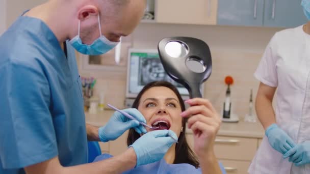 Munvårds undersökning för en mogen kvinna hon håller en spegel medan hennes tandläkare man gör muntliga kolla upp — Stockvideo