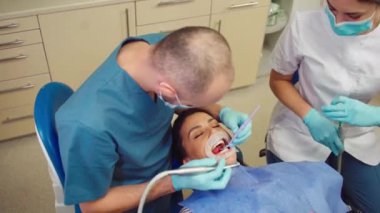 Modern diş hekimi ve asistanı büyük gülümsemesi olan olgun bir kadın için diş tedavisi yapıyorlar.