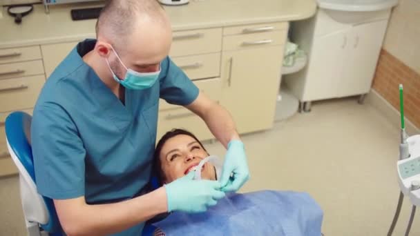 Стоматологічна клініка добре виглядає з великою посмішкою пацієнтка на сидінні стоматолога готується до пероральної перевірки стоматолога чоловік готується до лікування — стокове відео