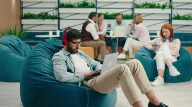 Çok zeki görünümlü, sakallı ve gözlüklü esmer bir adam laptopunda kulaklığıyla müzik dinlerken ve bir armut koltukta otururken ciddi bir iş yapıyor. Arri Alexa Mini.