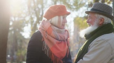 Soğuk bir sonbahar günü parkta yaşlı çiftler çok heyecanlı bir gezinti yapıyorlar kameranın önünde durup büyük bir gülümseme ve heyecan hakkında konuşuyorlar.