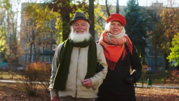 Πολύ casual και χαρισματικό ζευγάρι ηλικιωμένων σε ένα μεγάλο πάρκο στο κρύο au ημέρα αγκαλιάζει ο ένας τον άλλον ποζάρουν μπροστά από την κάμερα στέκονται ευθεία — Αρχείο Βίντεο