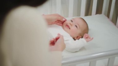 Gülümseyen küçük bir bebek bebek bebek karyolasında uzanırken annesine sarılıyor.