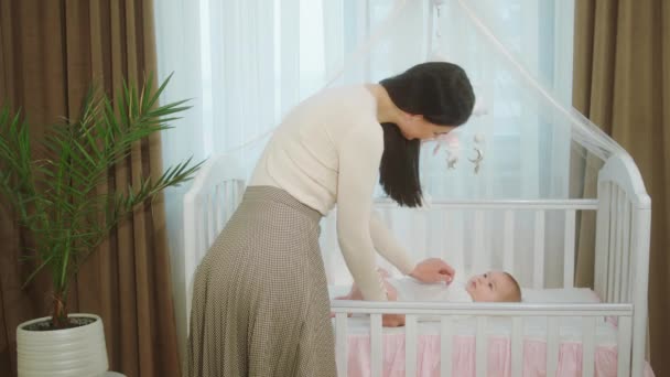 Koncepcja macierzyństwa i dzieciństwa młoda matka przyśpiesza czas ze swoją córeczką, podczas gdy dziecko kładzie się na łóżeczku niemowlęcym bardzo ostrożnie dotyka dziecka — Wideo stockowe