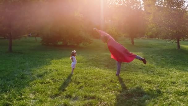Před kamerou roztomilé malé holčičky a jeho superhrdina táta hrát spolu uprostřed parku — Stock video