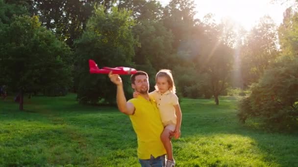 Im Park spielen der charismatische Mann und sein kleiner Sohn zusammen mit einem großen roten Flugzeug an einem sonnigen Tag mitten im Park — Stockvideo