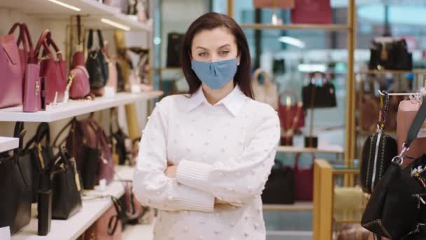 Delante de la cámara posando vendedora en la tienda de accesorios ha cruzado las manos y máscara protectora en la pandemia de coronavirus — Vídeos de Stock