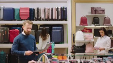Aksesuar dükkanından karizmatik bir yönetici eşyaların fiyatını kontrol etmek için dizüstü bilgisayar kullanırken diğer işçiler raftaki eşyaları düzenliyor.
