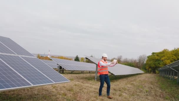 Fotovoltaik bataryaları modern güneş enerjisi istasyonunda kablosuz olarak kontrol etmek için dijital tablet kullanan çekici bir adam. 4k — Stok video