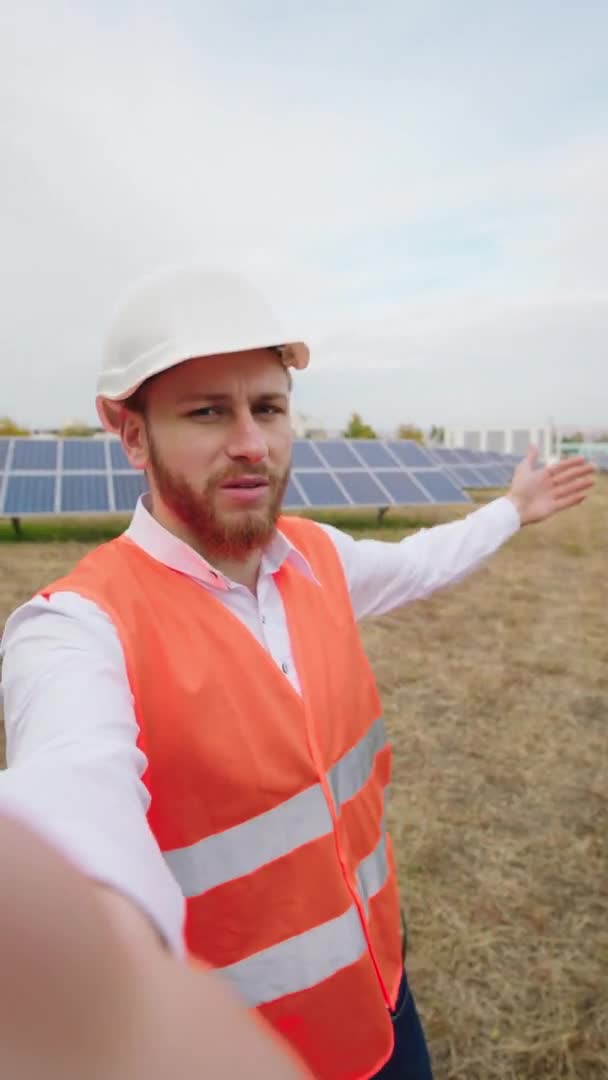 Pracownik ekologii w kasku bezpieczeństwa, nagrywający wideo, słoneczną elektrownię, mówiący o czymś, co pokazuje baterie fotowoltaiczne na końcu, pokazuje wielką, podobną i uśmiechniętą, dużą — Wideo stockowe