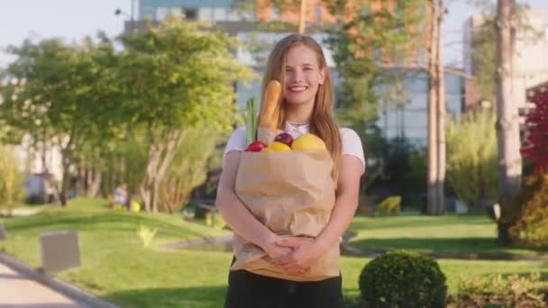 Charismatische dame met een grote glimlach in het midden van de moderne straat poseren voor de camera ze houdt een grote eco tas met voedsel — Stockvideo