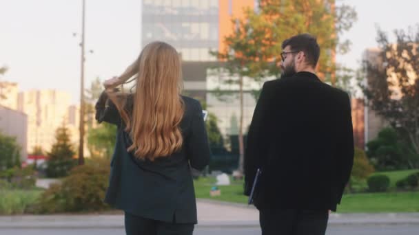 In a sunny day in the business centre park charismatic man and pretty lady office managers at the break time walking to the main business building using a tablet to analysing some tasks to do — Stock Video