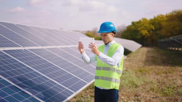 In een moderne grote zonne-energie boerderij jonge Aziatische ingenieur met behulp van digitale tablet om wat informatie te nemen over de zonnepanelen batterijen — Stockvideo