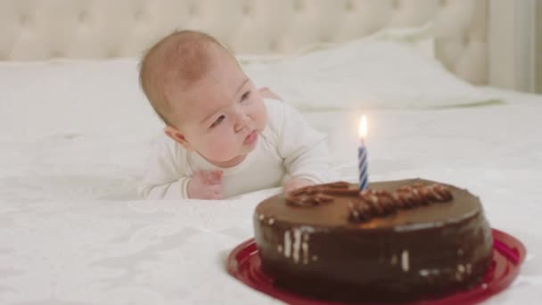 Charyzmatyczna ślicznotka leżąca na łóżku przed nią to duży tort czekoladowy ze świecą z przodu. — Wideo stockowe