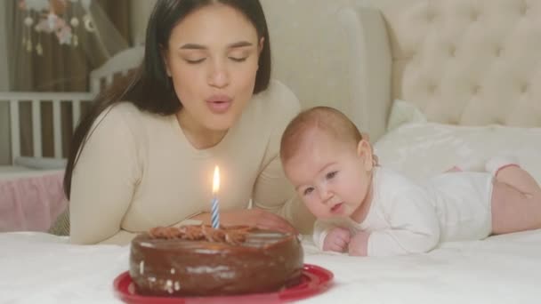 아름다운 어머니와 아기가 함께 침실에 있는 아기와 초콜릿 케이크에서 나온 촛불을 불고 있는 모습 — 비디오