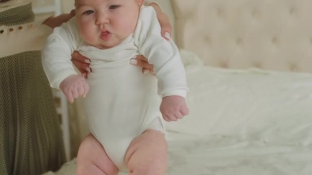 Vor der Kamera hüpft das süße kleine Mädchen glücklich über das Bett, während die junge Mutter das Baby vom Körper hält — Stockvideo