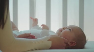 Güzel bir kız bebek karyolasına uzanmış, annesi kızıyla dikkatlice oynuyor, ellerine dokunuyor.