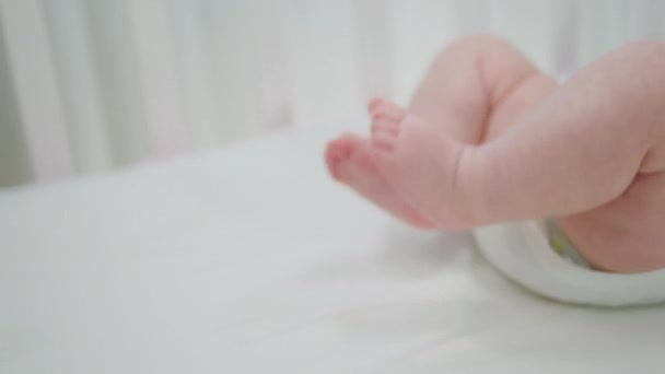 Fogalom a gyermekkor és az anyaság aranyos kislány feküdt a babaágyon, és mozog vele aranyos lábak részletek closeup — Stock videók