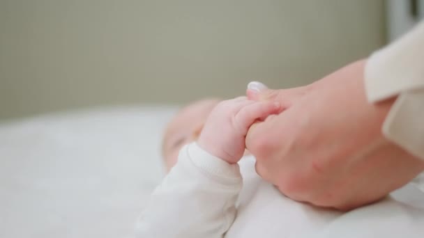 Delante de la cámara, el bonito bebé se siente feliz junto con su madre mientras se toma de la mano y se acuesta en la cama. — Vídeos de Stock