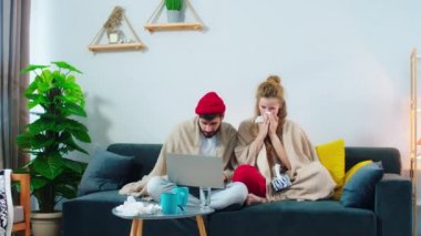 Kanepede oturan bir çift, ikisi de battaniyeye sarılı ve adam dizüstü bilgisayara bakıyor, kadın burnunu siliyor ve onu götürüyor. Kendini daha az hasta hissetsin diye ARRI Alexablets iğnesi vurulmuştu.