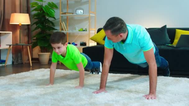 Papá y su pequeño hijo haciendo la tarea en casa en el suelo hacer flexiones duro y emocionado — Vídeo de stock