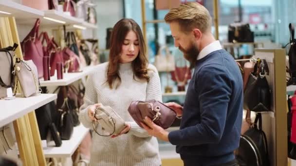 Egy nagy kiegészítők bolt csinos fiatal nő akar vásárolni egy táskát ő van egy beszélgetés az eladó megvitatják a különbség a táskák — Stock videók