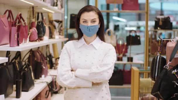 Portret van een mooie verkoopster met een beschermend masker die recht naar de camera kijkt en de handen kruist ze werkt een in de winkel met accessoires condor van kleine bedrijven en ondernemer — Stockvideo