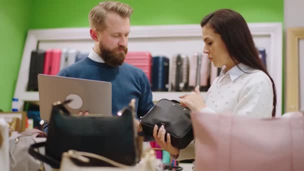 In de accessoire winkel supervisor samen met verkoopster analyseren van nieuwe tassen uit de winkel en maak een aantal notities op de laptop — Stockvideo