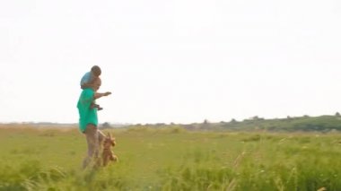 Tatlı küçük çocuk babasının sırtında koşuyor ve sevimli küçük köpekleri İngiliz cocker spaniel ile oynuyorlar.