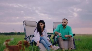 Güzel bayan ve partneri doğada piknik yapıyorlar sandalyelere oturup şirin küçük bir köpekle oynuyorlar İngiliz cocker spaniel rase