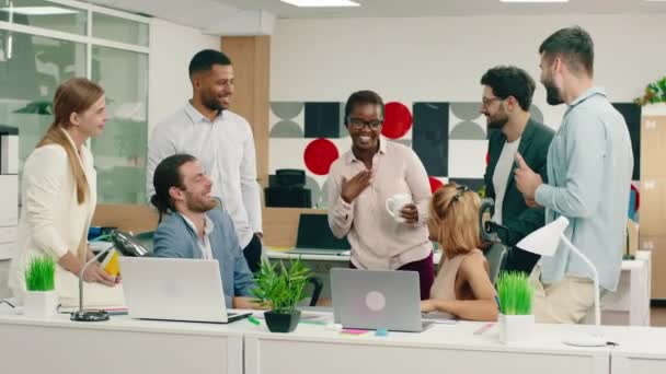 大規模なオフィスセンターの多民族オフィスの労働者やマネージャーは、彼らはすべての人に面白い話をして美しい黒の女性を笑っている会話を持っています — ストック動画