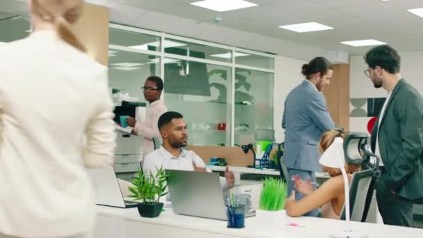 Atraktivní obchodník s vlasy svázanými dozadu vejde na schůzi v kanceláři, plácne si s každým a dostane ukázku odvedené práce — Stock video