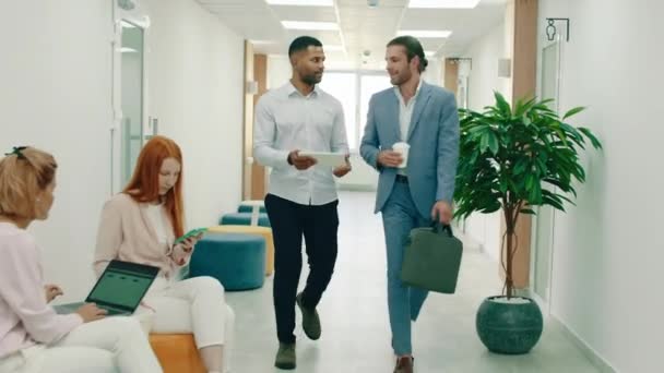 ビー玉を持つ2つの重要な外観の男性は、ビジネスの話をしながら、大規模なオフィスを介して人々を渡すと、彼らは両方のスーツを着ていると非常にインテリジェントに見えます。Arri Alexa Mini. — ストック動画