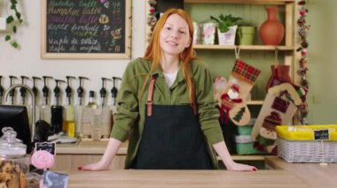 Kahve dükkanının masasında dikilirken kameranın önünde dans eden ve gülümseyen harika genç barista kadın.