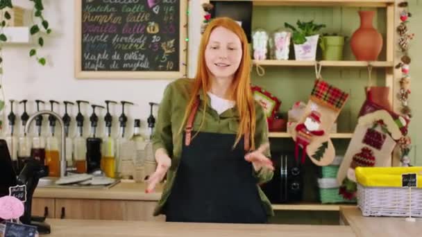 Karismatisk med ett vackert leende barista dam poserar framför kameran passerar händerna på kaféet hon har ett gott humör väntar på kunden — Stockvideo