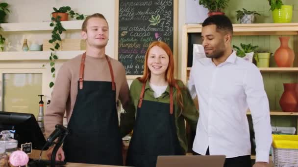 Team multietnico nella caffetteria due baristi e il proprietario in posa davanti alla telecamera si abbracciano e sorridono carino — Video Stock