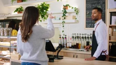 Terminal masasında çalışan Afro-Amerikan kahve dükkanındaki kameranın önünde müşteri bayanla tartışıyor ve siparişi alıyor.