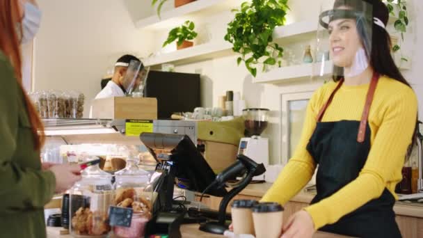 Belle femme barista avec un grand sourire donnant l'ordre à la cliente au café toutes les choses et le client portant des masques de protection dans la pandémie de coronavirus. 4k — Video