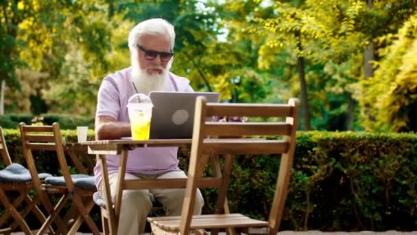 Σε μια ηλιόλουστη μέρα γέρος πολύ ελκυστικός Ξύπνησε στο laptop του πληκτρολογώντας κάτι που φοράει γυαλιά ηλίου — Αρχείο Βίντεο