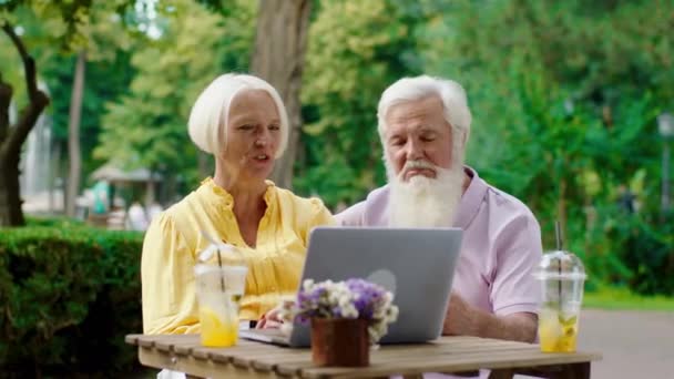 In het midden van het park in het cafe oud uitziende man en vrouw hebben een romantische tijd op zoek naar de laptop iets en snelheid goede tijd samen — Stockvideo