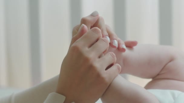 Anyaság és gyermekkor koncepció a kamera előtt közelkép fiatal anya kezét játszik a baba lábát reggel — Stock videók