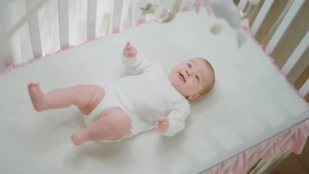 Sehr aufgeregtes kleines Mädchen genießt die Zeit in ihrem Babybett allein sie bewegt sich mit ihren niedlichen Beinen und schaut sich Kinderspielzeug an — Stockvideo