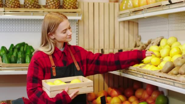 Friska livsstil koncept stilig dam bonde i grönsaksaffären håller en kista full av citron och ersätta dem till trähyllor — Stockvideo